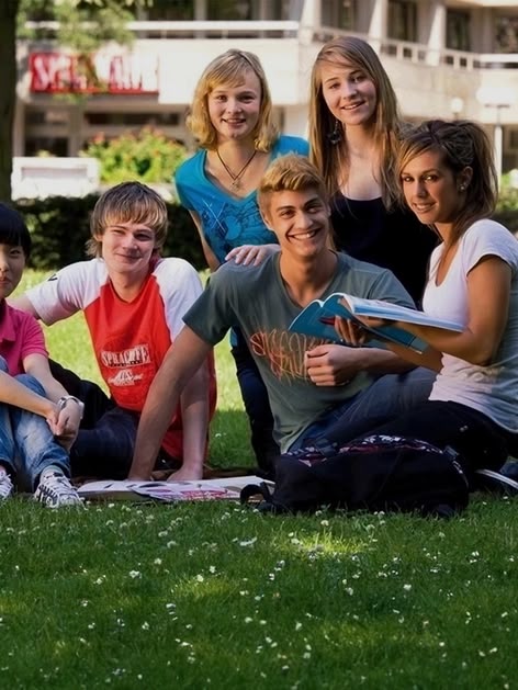 Group of Sprachcaffe junior students sitting on the grass in Frankfurt, Germany, smiling and enjoying a sunny day.