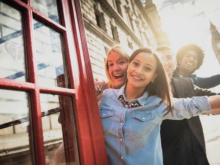 Smiling girl posing by a red phone booth in London with Big Ben visible in the background.