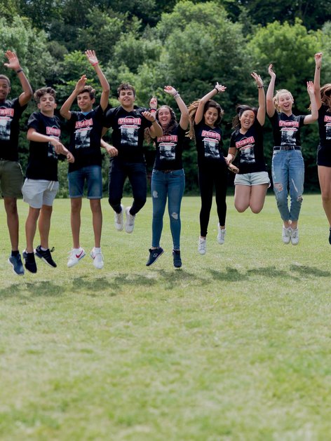Sprachcaffe students in England jumping mid-air on a green field, wearing matching shirts and enjoying the outdoors.