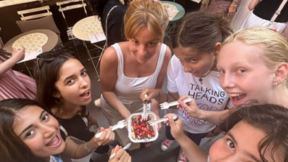 Group of smiling girls sharing a dessert on a street in Nice, France, in front of a café.